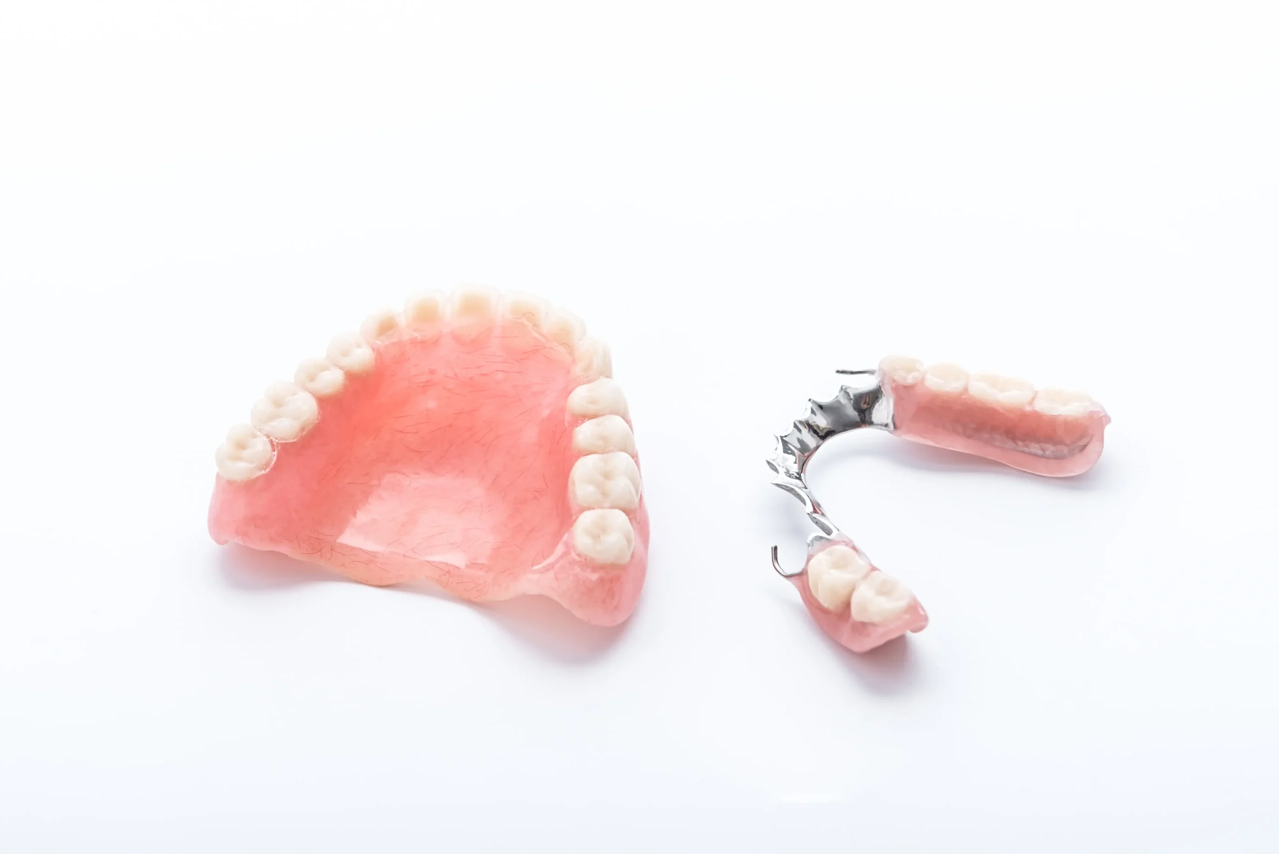 Crown Dental Group - A set of pink dentures and a partial metal denture rest on a white background. The dentures display realistic-looking teeth, conveying a clinical tone.